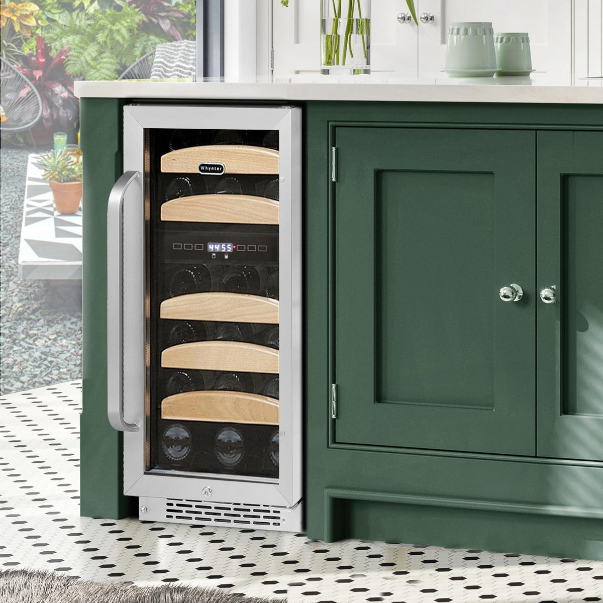 Wine cooler integrated into a green kitchen cabinet with a view of outdoor furniture.