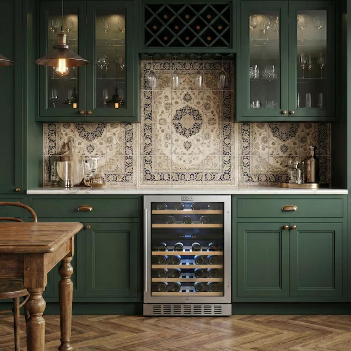 A built-in wine refrigerator in a dark green kitchen cabinetry setup with patterned tile backsplash, glass-front cabinets, pendant lights, and a wooden dining table partially visible.